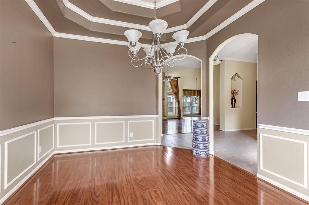 Elegant office space featuring rich wood flooring, classic wainscoting, and a stylish tray ceiling with a sophisticated chandelier, offering a perfect blend of functionality and charm.