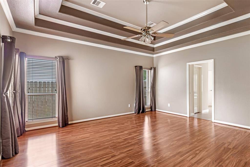 Spacious primary bedroom featuring elegant tray ceilings, abundant natural light, and rich wood flooring.