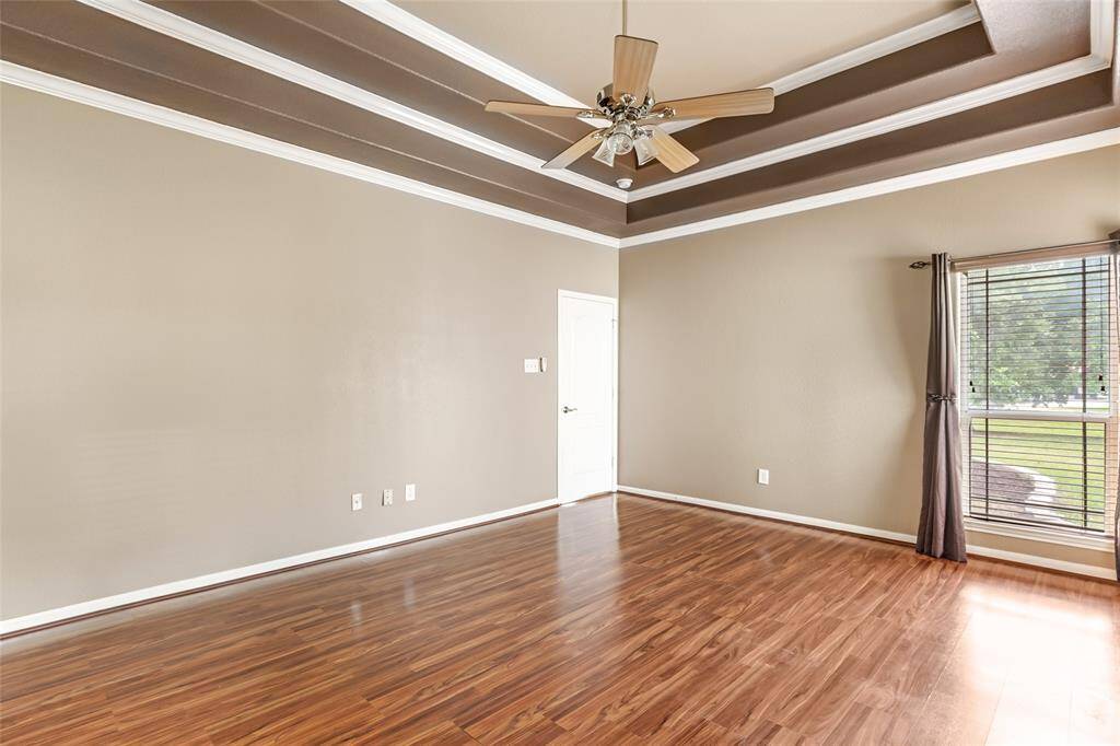 Spacious primary bedroom featuring elegant tray ceilings, rich hardwood floors, and abundant natural light from a large window.