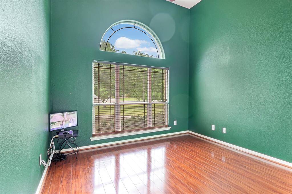 Bright and inviting, this second bedroom features a high ceiling, rich wood flooring, and a large arched window with scenic views. Perfect for relaxation or a home office.