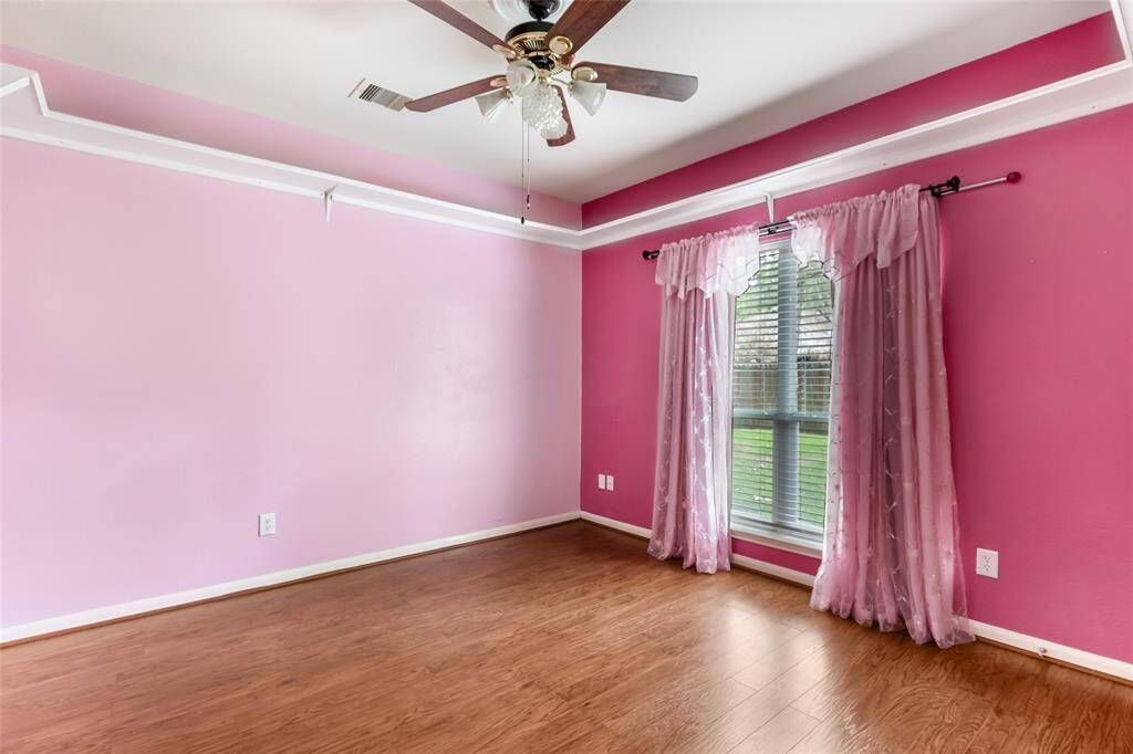 This vibrant fourth bedroom features wood flooring, a ceiling fan, and ample natural light, offering a cozy and inviting space.