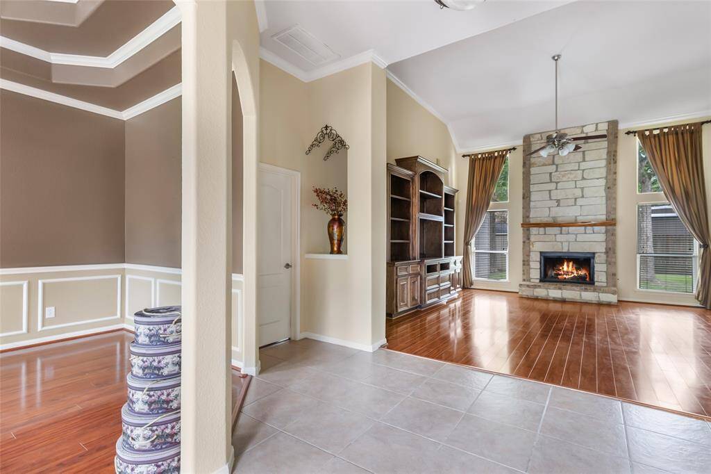 Welcome to a foyer that seamlessly transitions into a spacious living area, featuring elegant wood flooring, a cozy stone fireplace, and abundant natural light through large windows.