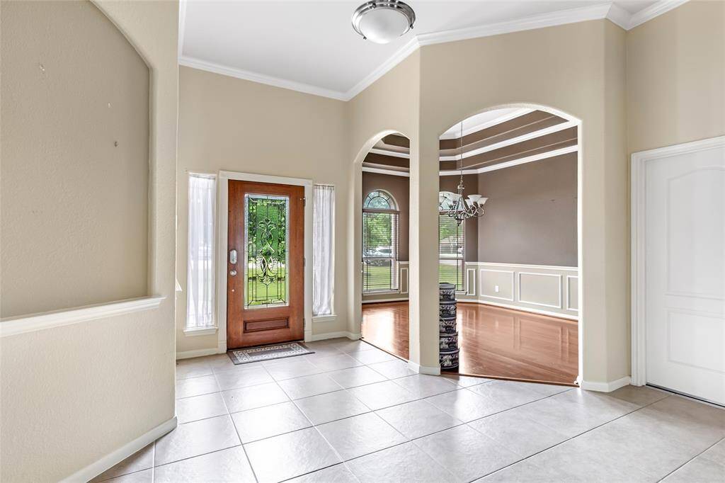 Welcome to a stunning entryway featuring elegant tile flooring, high ceilings, and an ornate glass door. Arched openings lead to a spacious dining area with rich hardwood floors, creating a warm and inviting atmosphere.