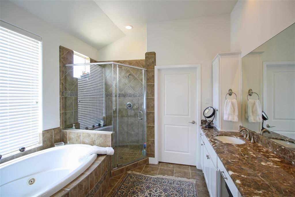 Pristine Primary Bath offers double sinks, and elongated vanity with seating area, dual built-in cabinets, oversized jacuzzi tub, glass enclosed shower with bench seating, and private water closet.