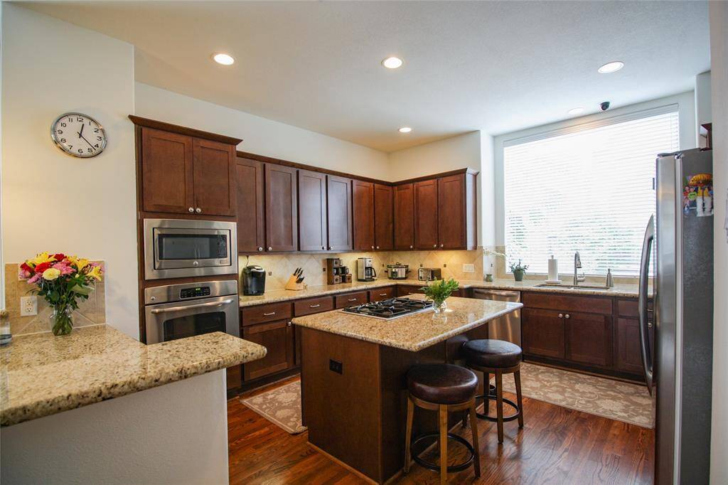 Island kitchen with rich toned wood shaker cabinetry, granite countertops, gas cooktop, & stainless steel appliances. The incredible picture window allow for natural light.