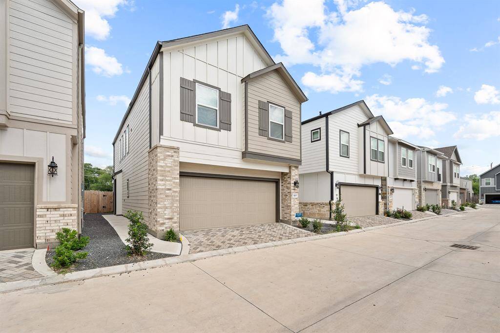 Modern, low-maintenance home with sleek light siding and brick accents. Features include a two-car garage, charming landscaped areas, and a shared driveway. Perfect for those seeking contemporary living.