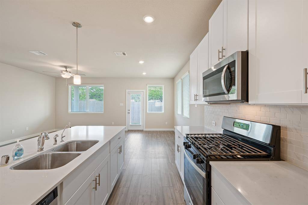 Bright and modern kitchen with stainless steel appliances, white cabinetry, and a large island. The open layout flows into a spacious living area with natural light from multiple windows.