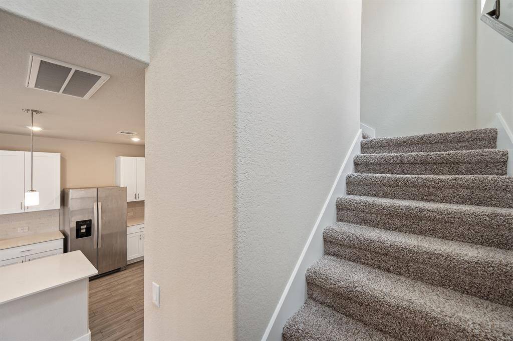 This photo features a modern kitchen with white cabinetry and stainless steel appliances, adjacent to a carpeted staircase leading to the upper level. The space is well-lit and has a clean, contemporary feel.