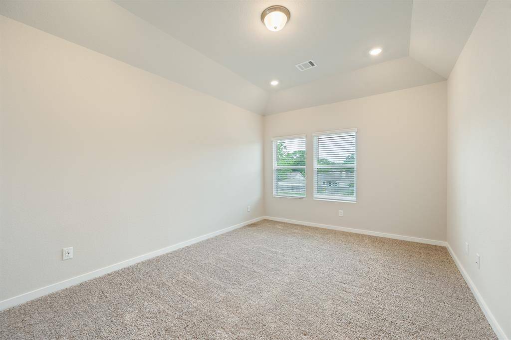 This is a bright, carpeted room with neutral walls, recessed lighting, and a central ceiling fixture. It features two windows that let in natural light, making it feel spacious and inviting.