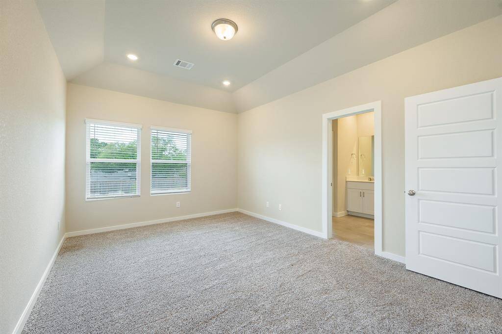 This is a bright, spacious bedroom featuring neutral walls, carpeted floors, and a ceiling light. It has two windows for natural light and an en-suite bathroom with a modern vanity.