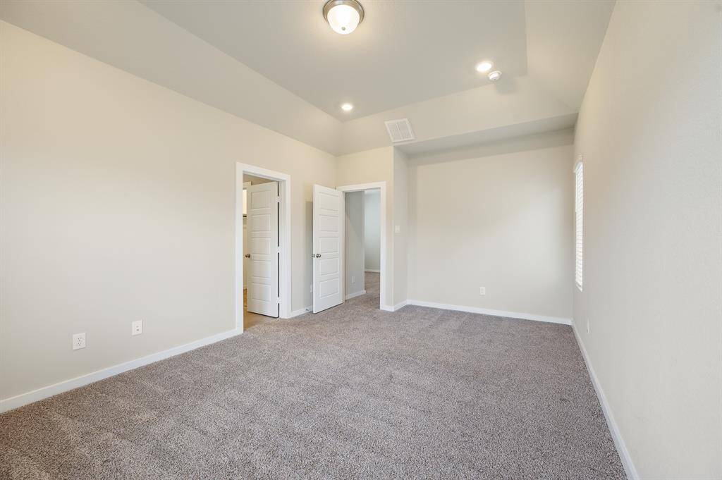 This photo showcases a spacious, carpeted room with neutral walls, perfect for a bedroom. It features a high ceiling with recessed lighting and two doorways, providing ample natural light from a side window.