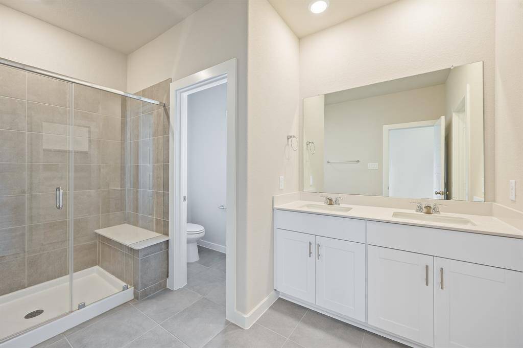 This bathroom features a spacious walk-in shower with glass doors, a double vanity with ample storage, and a large mirror. The neutral color palette and recessed lighting create a bright and modern atmosphere.