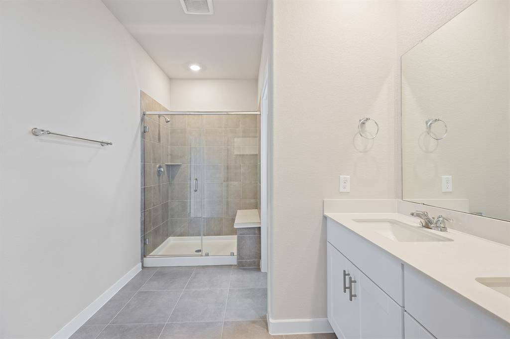 This modern bathroom features a spacious glass-enclosed shower with tiled walls and a built-in bench. It includes a sleek double vanity with ample storage and a large mirror, offering a clean and bright space.