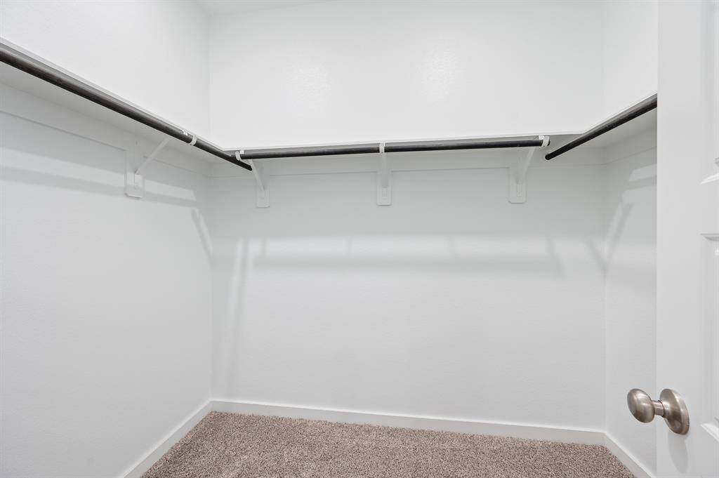 This is a spacious, well-lit walk-in closet with multiple hanging rods and fresh white walls, providing ample storage space. The carpeted floor adds a touch of comfort.