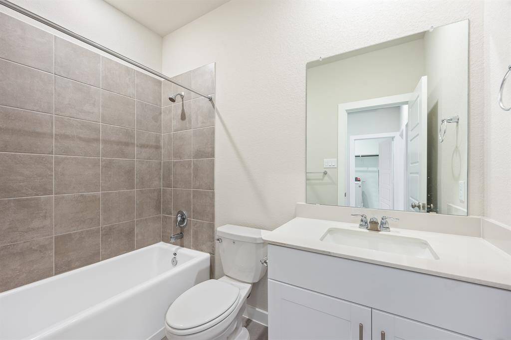 This bathroom features a clean, modern design with a bathtub-shower combination, beige tiled walls, a white vanity with a large mirror, and neutral tones throughout.