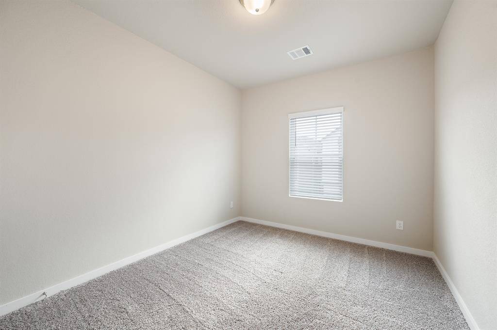 This photo shows a small, neutral-toned room with carpeted floors and a window with blinds, ideal for a cozy bedroom or home office.