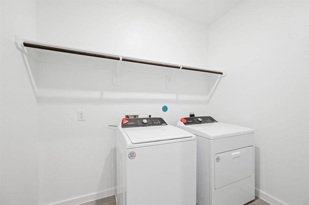 This photo shows a clean, bright laundry room with a washer and dryer. It features a white wall with a utility shelf above the appliances for extra storage.