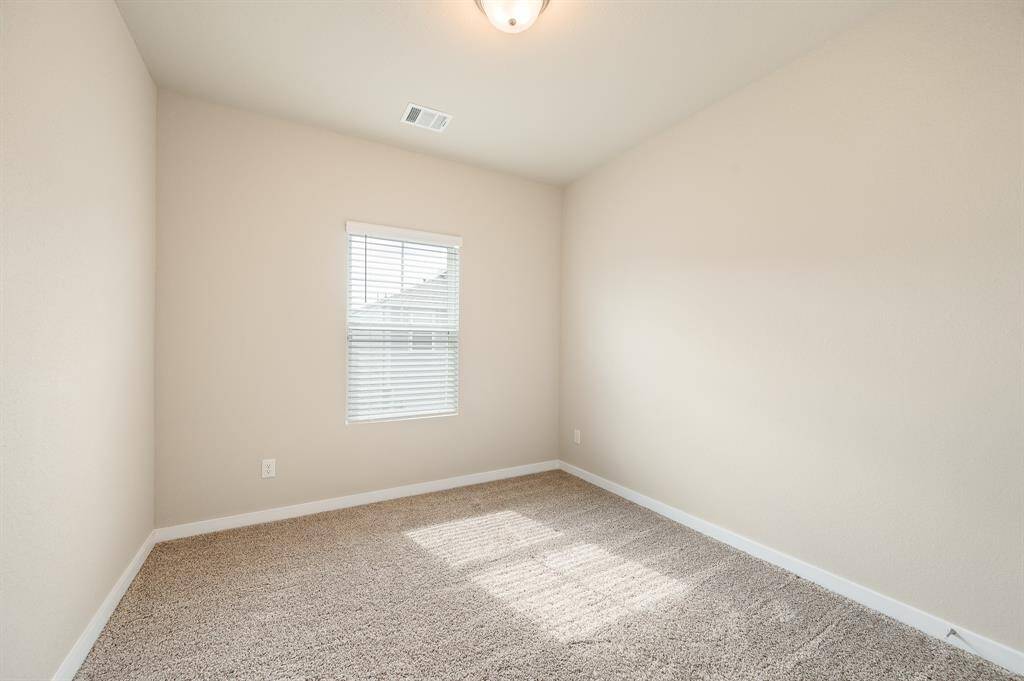 This is a cozy, well-lit room with beige walls, carpeted flooring, and a window with blinds, ideal for a small bedroom or office space.