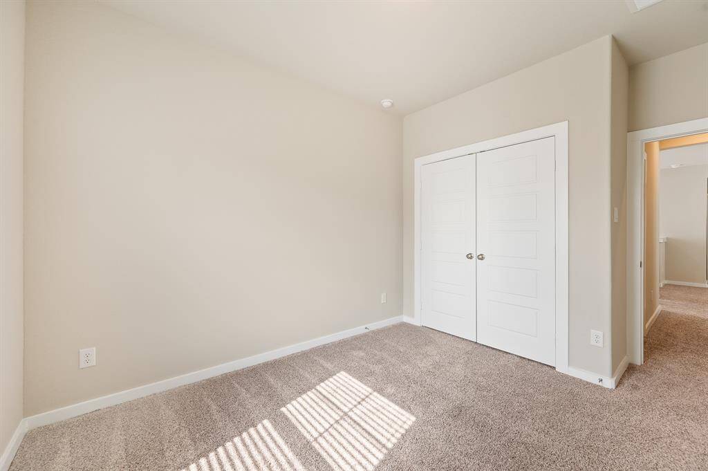 This is a bright, carpeted bedroom with neutral-colored walls and a double-door closet. The room receives ample natural light through a window, creating a warm and inviting atmosphere.