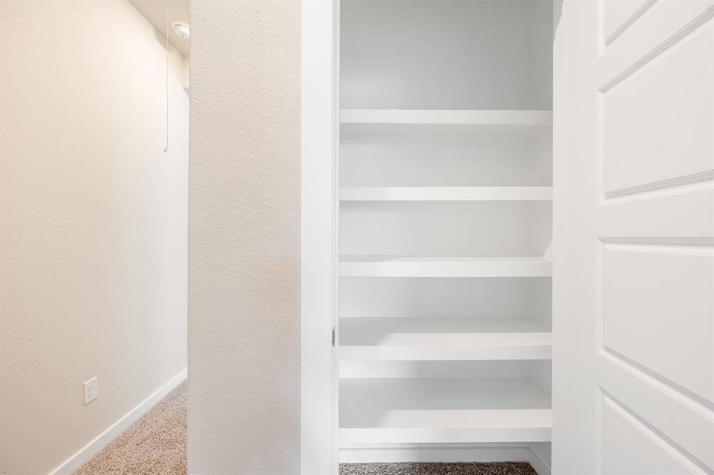 This photo shows a well-lit hallway with a built-in, open shelving unit perfect for storage. The space features carpeted flooring and neutral wall colors, offering a clean and functional area.