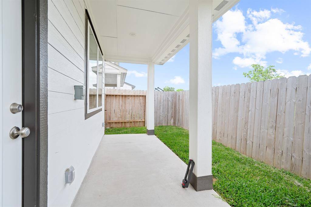 This photo showcases a covered patio area with a concrete floor, adjacent to a grassy yard enclosed by a wooden fence. It's a bright, inviting space perfect for outdoor relaxation or entertaining.