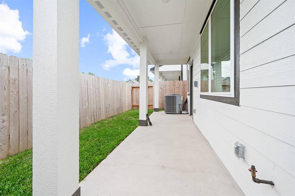 This photo shows a covered patio area with a concrete floor, adjacent to a white house exterior, overlooking a small green lawn. It's bordered by a wooden privacy fence, providing a cozy outdoor space.