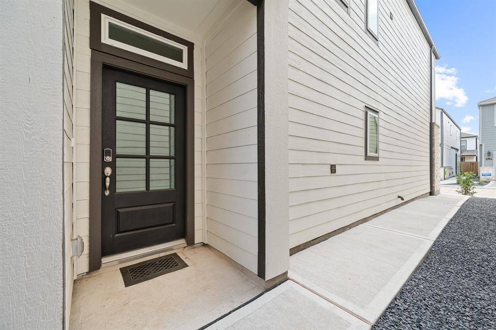 Discover modern elegance with this home's chic black door with glass panes, set against light siding and a sleek concrete walkway.