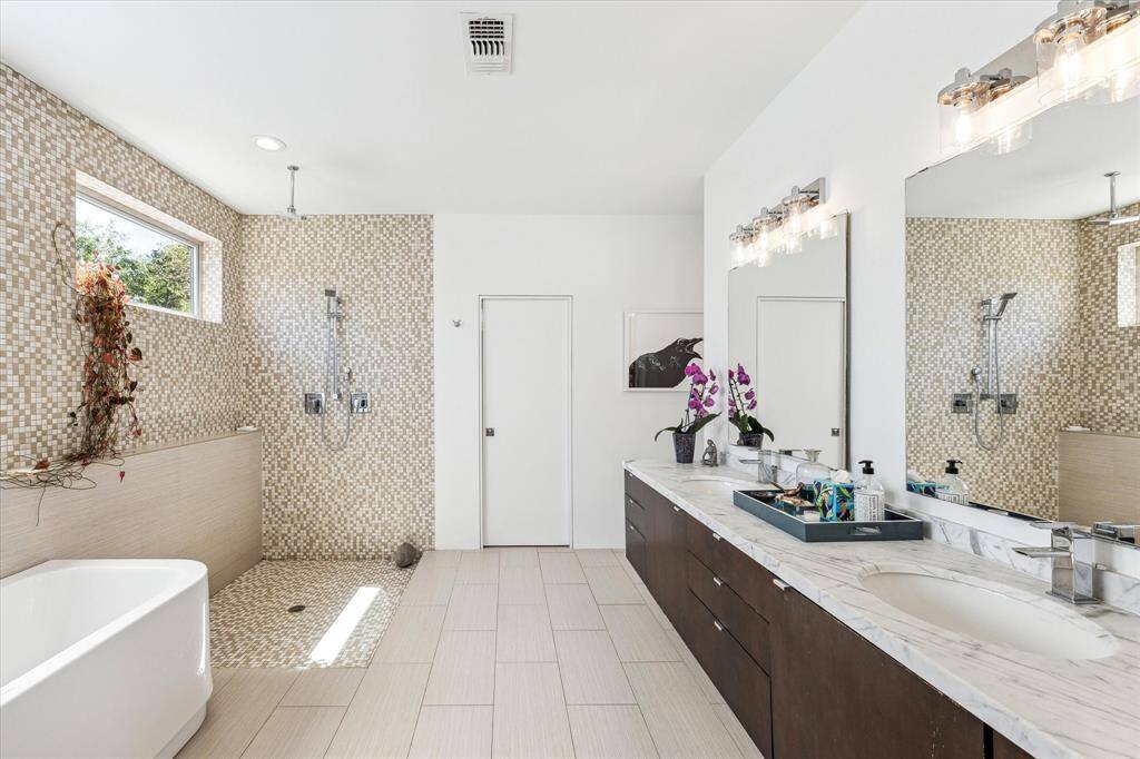 Experience indulgence in this modern bathroom with a large, open shower featuring a rainfall & hand-held showerhead and mosaic tiles.  Clean lines and natural materials create a serene ambiance, perfect for unwinding.