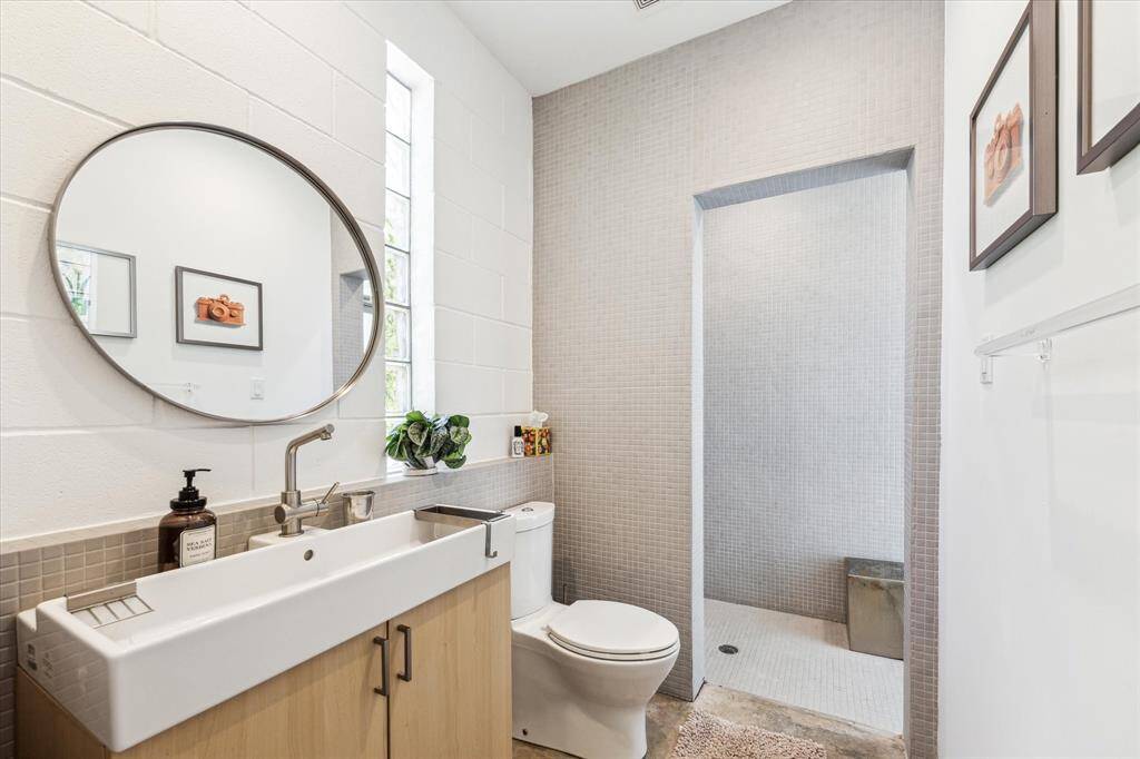 The ensuite bathroom has a contemporary style with a rectangular vessel sink, concrete floors, and walls of mosaic tile which lead to the walk-in shower. This washroom also serves as the pool bathroom w/ direct access outdoors.