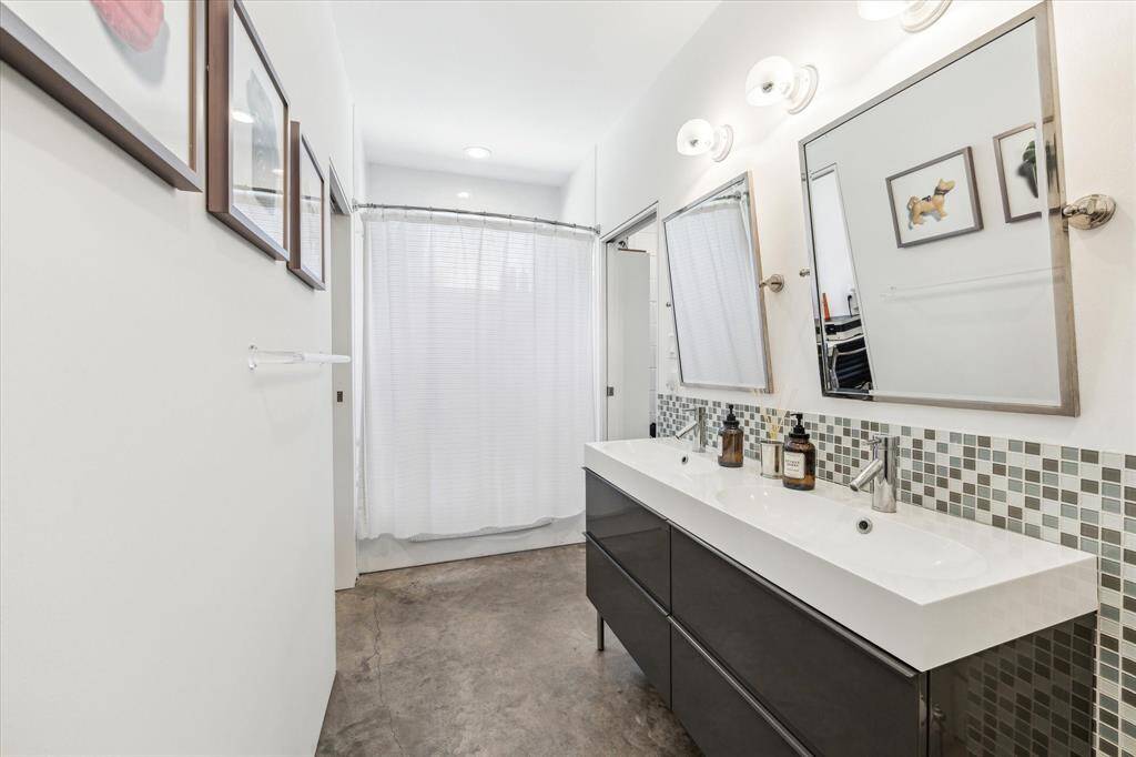 Guests will have plenty of elbow room in this shared bathroom showcasing dual sinks, chrome framed tilting mirrors, mosaic accent tile, retro wall lights and a tub/shower combo.
