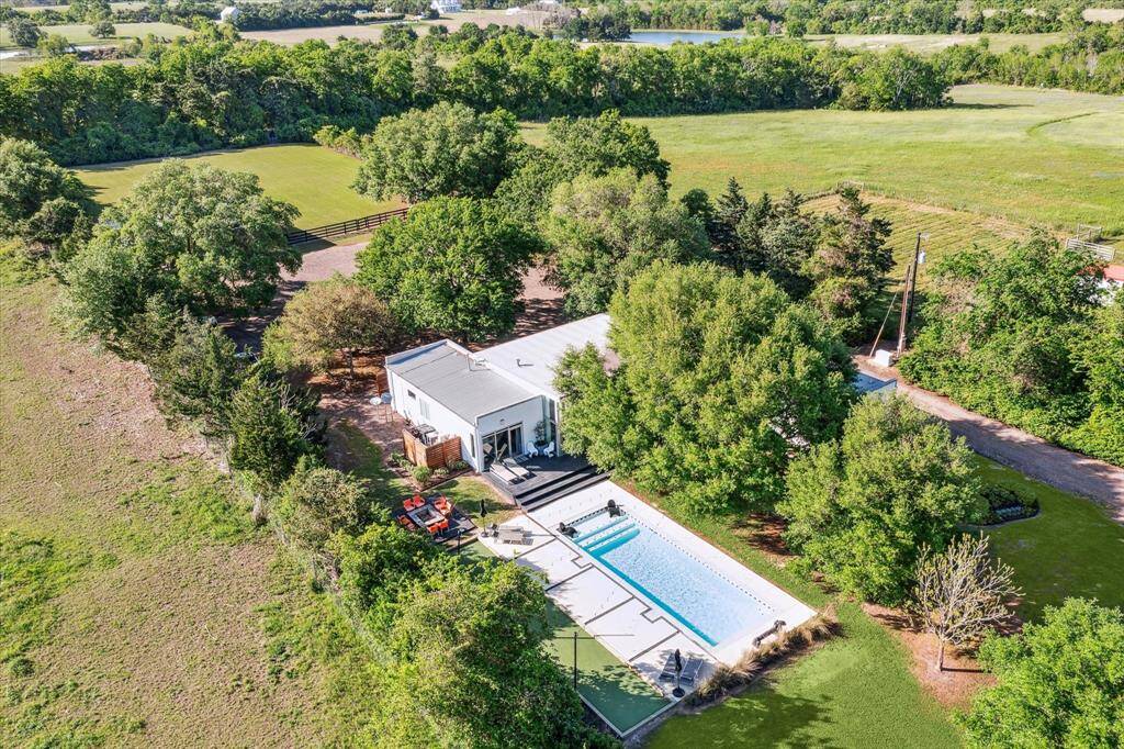 An aerial view of the home, pool, sun deck, firepit, bocci ball court and back pasture, you can see it's nestled among trees. The property offers tranquility and privacy, making it an ideal retreat from the hustle and bustle of everyday life.