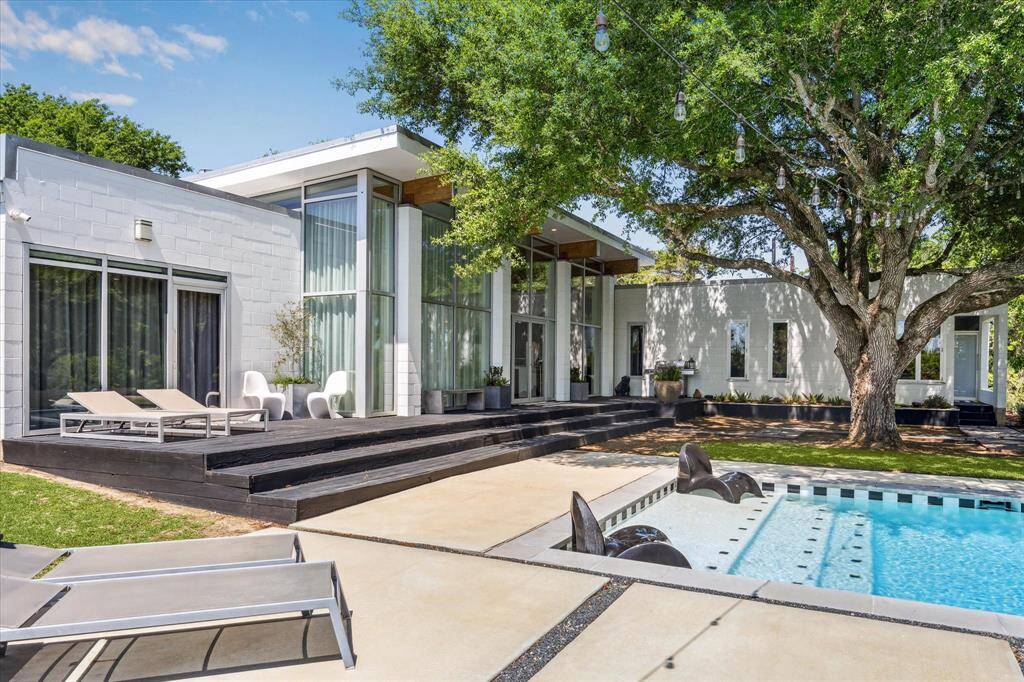 This view captures the back side of this stunning home. Notice all the glass surrounding the main entertaining space and the door on the deck which leads to the primary suite. The first step of the pool is "the spot" for sunbathing and staying cool at the same time!