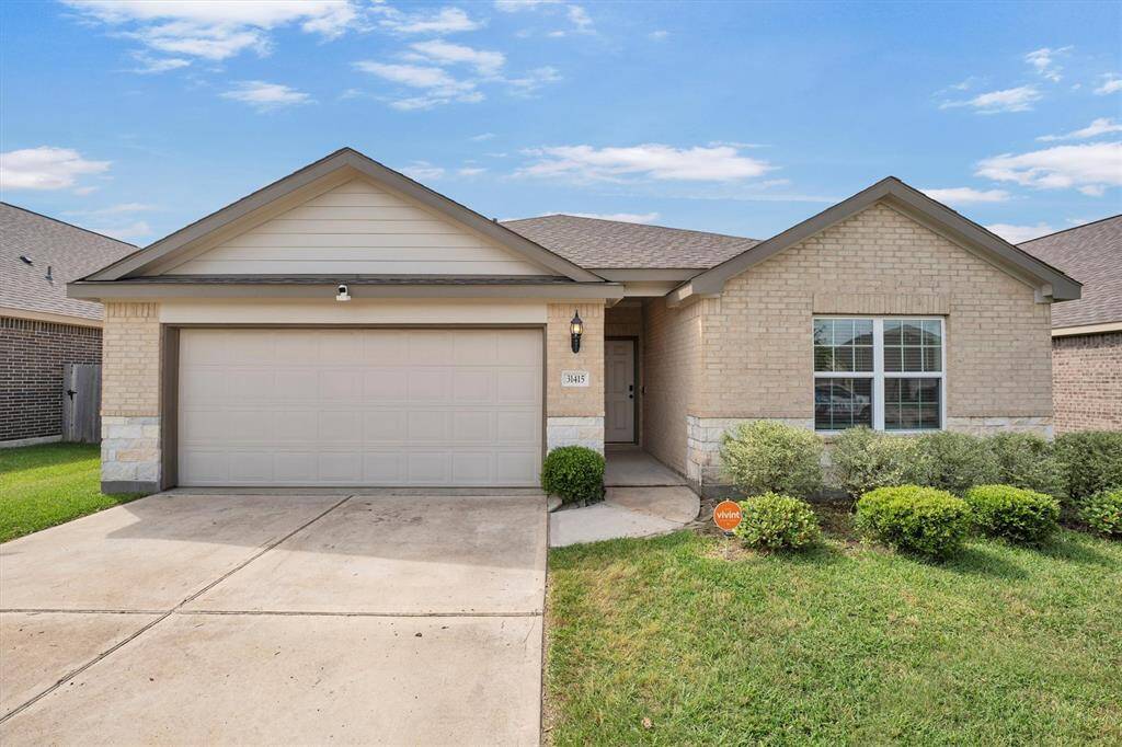 Welcome to 31415 Stone Ridge Forest Dr. A modern suburban home with a neatly maintained front lawn, a two-car driveway, and a covered entryway. The neighborhood is well-kept, with similar style houses and green spaces, offering a clean and welcoming environment.