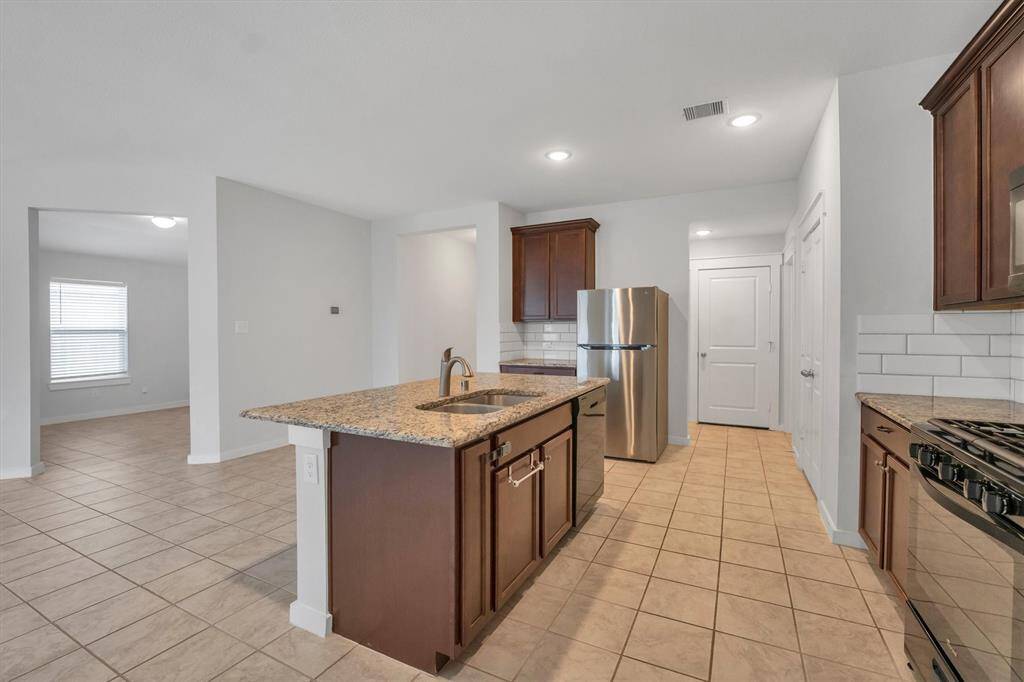 This kitchen features modern appliances, granite countertops, and a central island with a sink. It has ample cabinet space and a tiled floor, leading into an open living area with natural light.