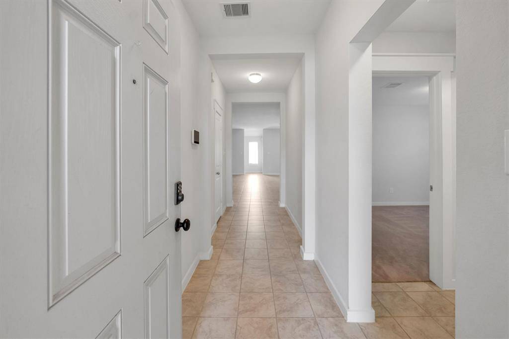 This photo shows a bright, long hallway with tile flooring, leading to an open living area. It features a classic white door and neutral walls, providing a clean and welcoming entrance.