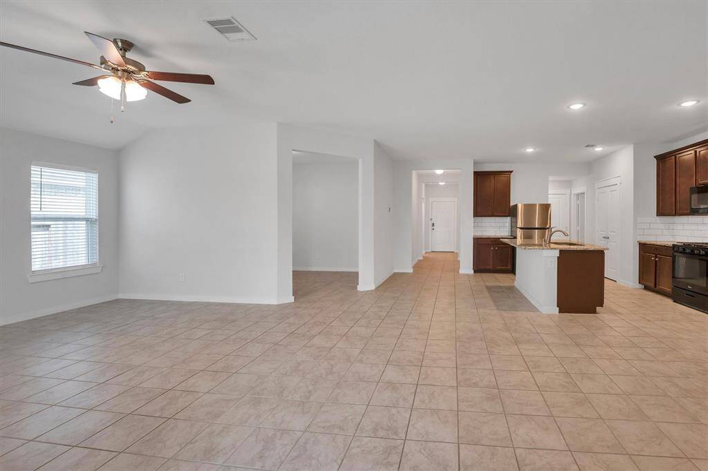 This spacious, open-concept area features a modern kitchen with black appliances, stainless steel refrigerator, dark wood cabinetry, and a center island. The living space has large windows, a ceiling fan, and tile flooring throughout, creating a bright and inviting atmosphere.