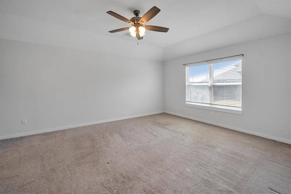 This spacious bedroom features neutral carpeting, a large window for natural light, and a ceiling fan for comfort.