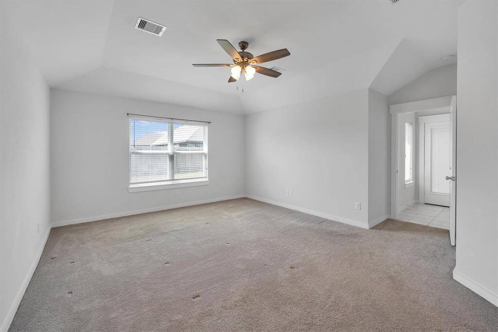 The primary bedroom features neutral carpeting, a ceiling fan, and a large window for natural light. It has a vaulted ceiling, and an adjacent doorway leading to the patio door and close to the Kitchen/Breakfast room area.