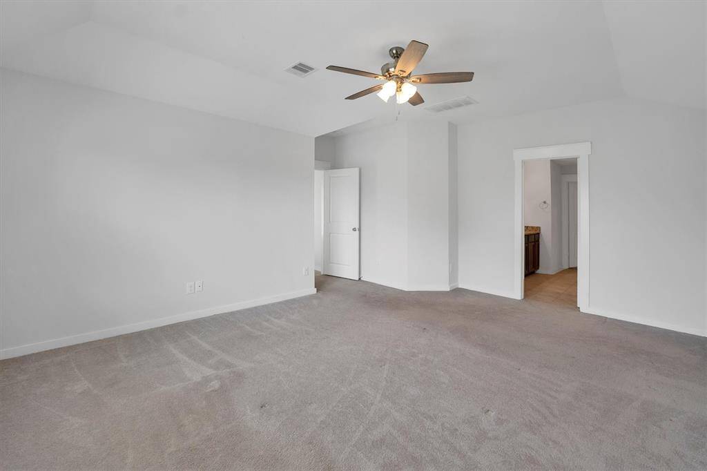 This spacious primary bedroom features neutral carpeting, a ceiling fan, and ample natural light. It includes a doorway leading to an en-suite bathroom, enhancing convenience and privacy.