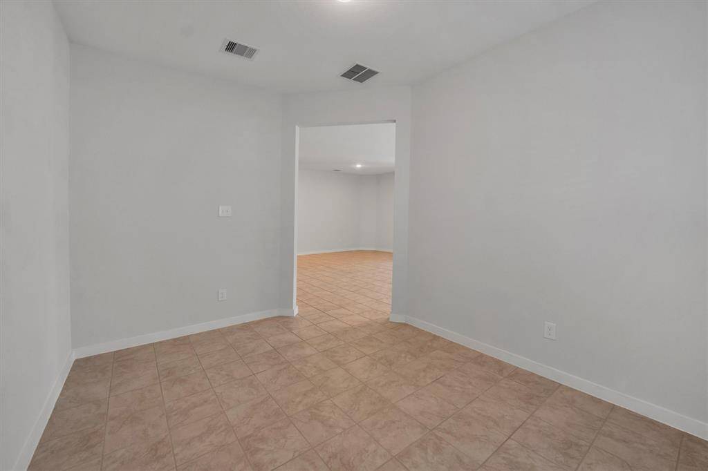 This photo shows a room with light-colored walls and tiled flooring, leading to another open area. The space is well-lit and has a clean, neutral design, ideal for versatile use.