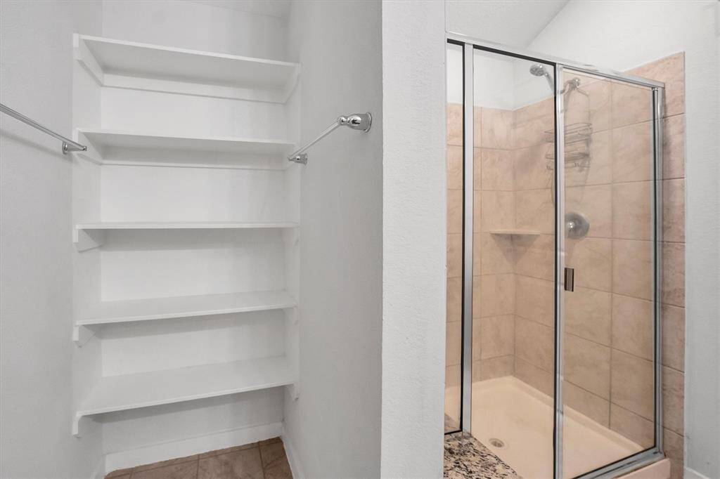 Primary bath offers a tiled walk-in shower featuring glass doors. Adjacent to the shower, there are built-in white shelves for storage, along with a towel bar, providing convenience and functionality.