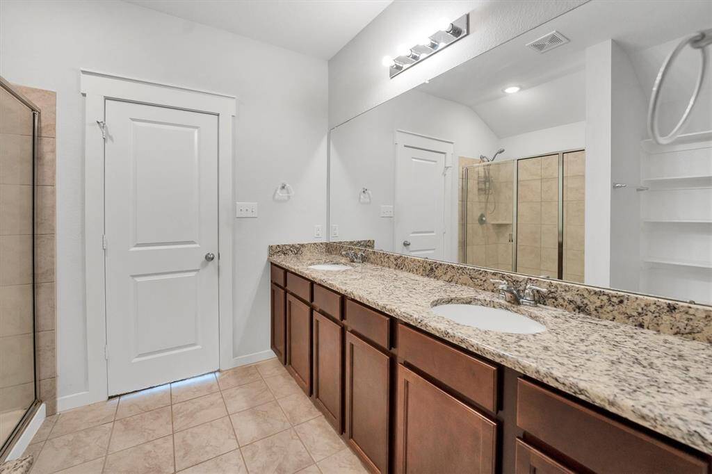 This photo showcases a modern bathroom with dual sinks set in a granite countertop, dark wood cabinets, and a walk-in shower. The neutral tile flooring and ample mirror space create a spacious and elegant atmosphere.