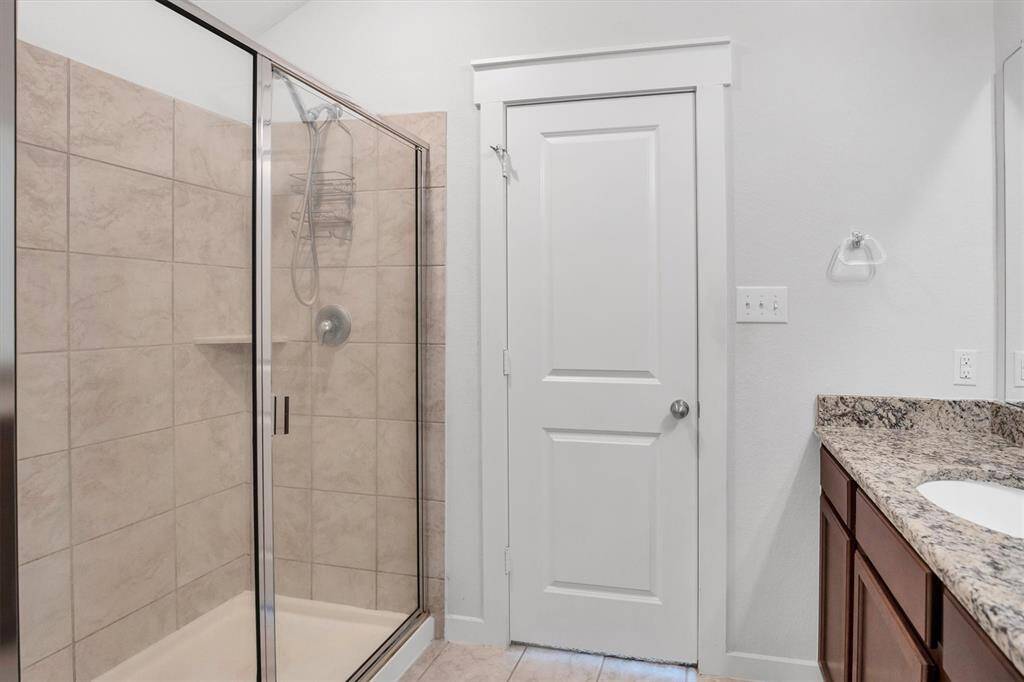 Primary bathroom with a spacious tiled shower, granite countertop, and wooden cabinetry.
