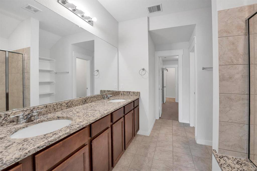 Primary Bath features a spacious double vanity with granite countertops, a large mirror, and ample cabinet storage. It includes a tiled shower and light tile flooring, creating a clean and modern look.