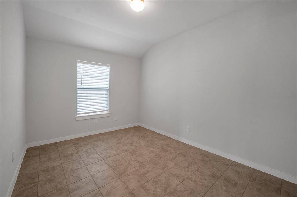 This room features neutral walls, a single window with blinds, and tiled flooring, creating a bright and versatile space.