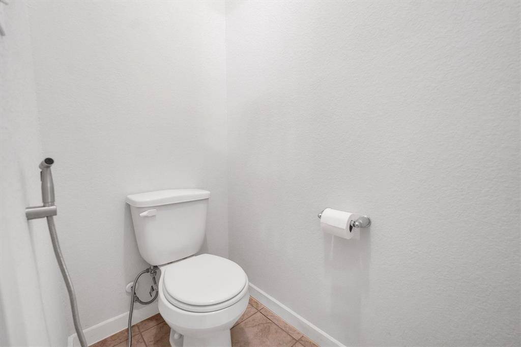 Compact, clean bathroom featuring a toilet, handheld bidet, and simple tile flooring.