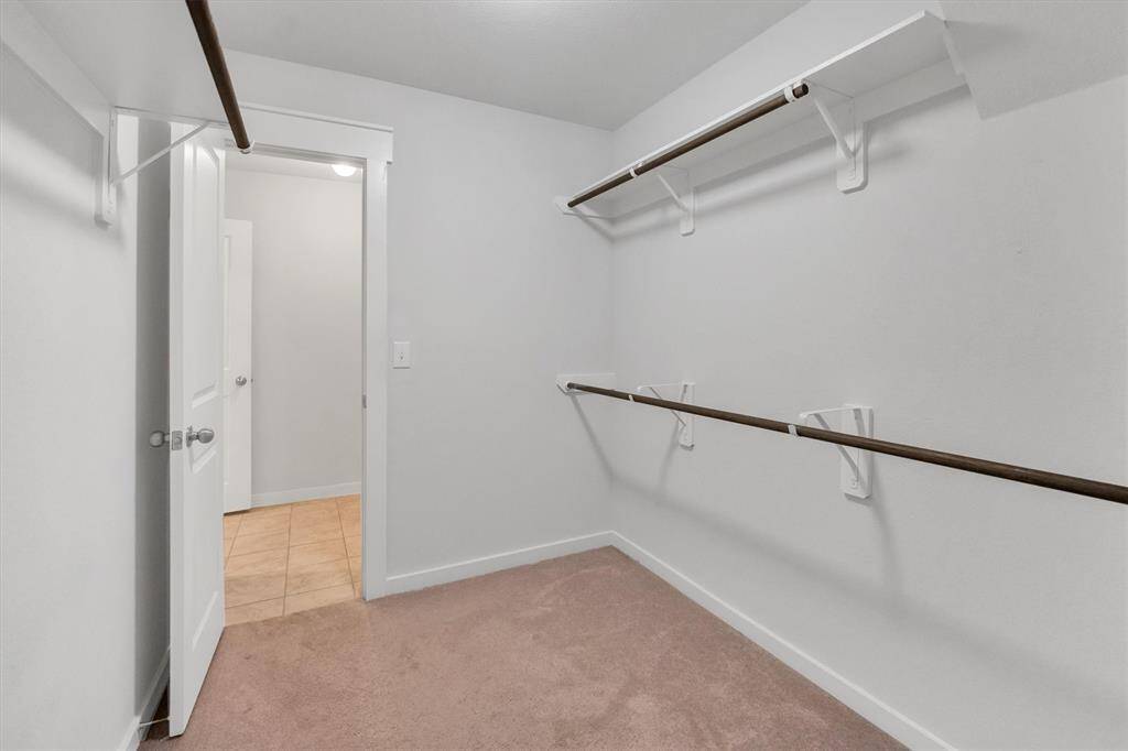 Primary Bedroom walk in closet offers a spacious walk-in closet with multiple hanging rods, neutral carpet, and white walls, providing ample storage space.