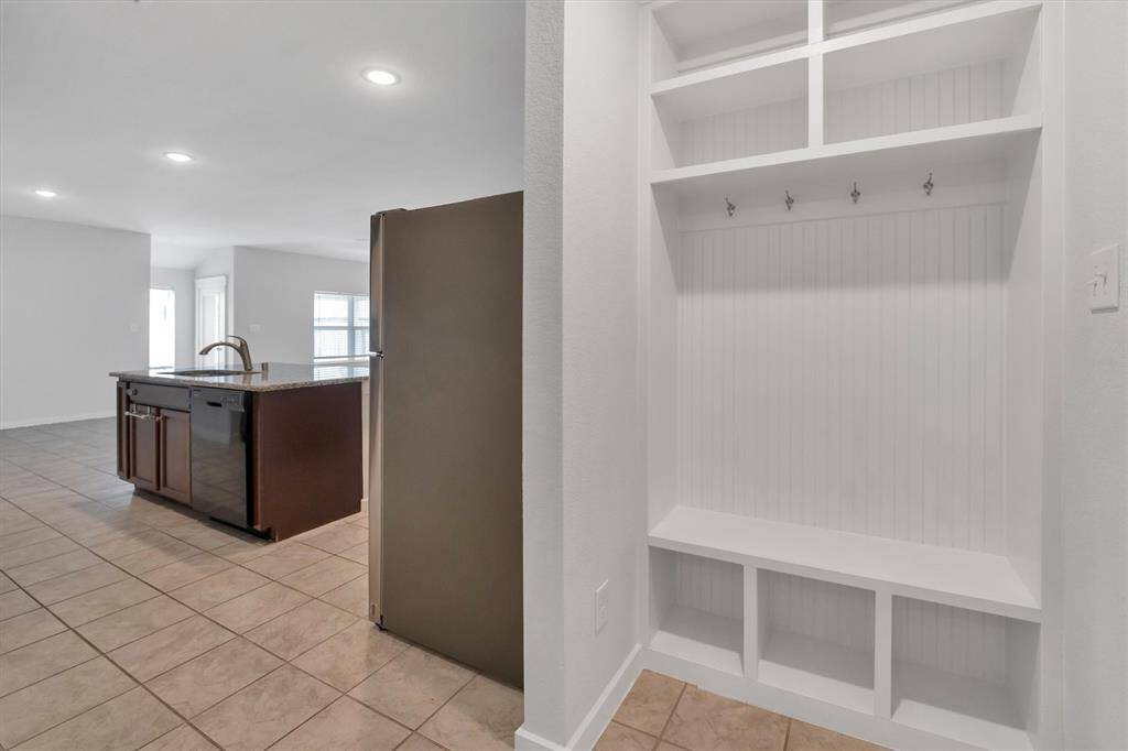 Another view of the spacious kitchen with tile flooring, featuring a large island with a sink and dishwasher. It opens into a bright, airy living area. To the side, there’s a built-in mudroom bench with storage and hooks, perfect for organization.