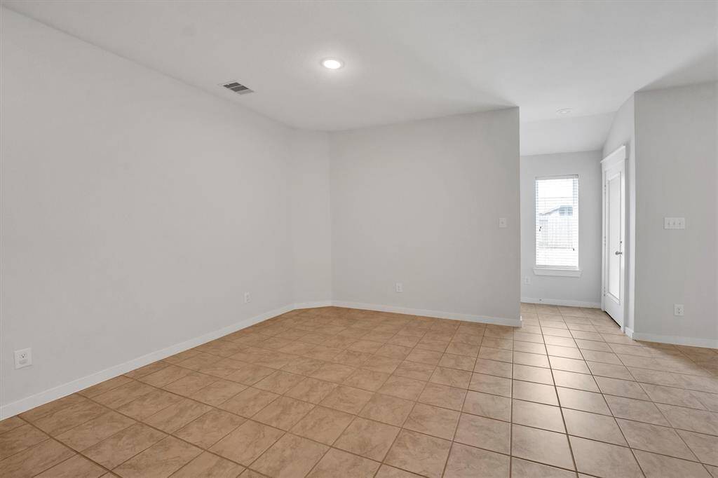 This photo shows a bright, secondary bedroom with neutral walls and tiled flooring. It features a small window and a door, creating a simple and versatile space.
