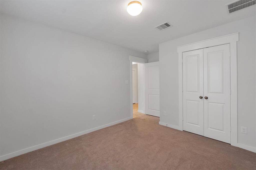 This is a secondary bedroom, carpeted bedroom with neutral walls and a ceiling light. It features a double-door closet and an open doorway leading to another area of the home.